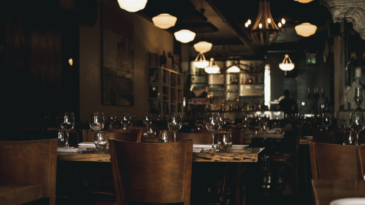 An upscale, warmly lit restaurant dining room with wooden tables set with wine glasses, representing the high-quality commercial kitchens in Northern Virginia that utilize Ember and Oak's cutting board rental and exchange service.